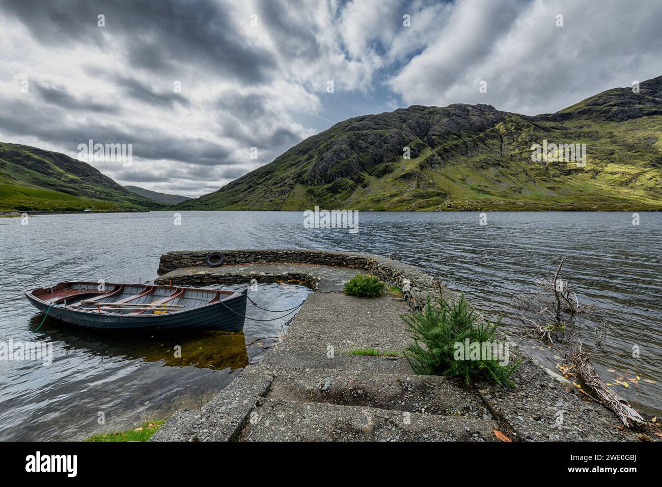 Landscape of a stone jetty with some wooden boats on a river in the East of Ireland with cloudy sky Stock Photo