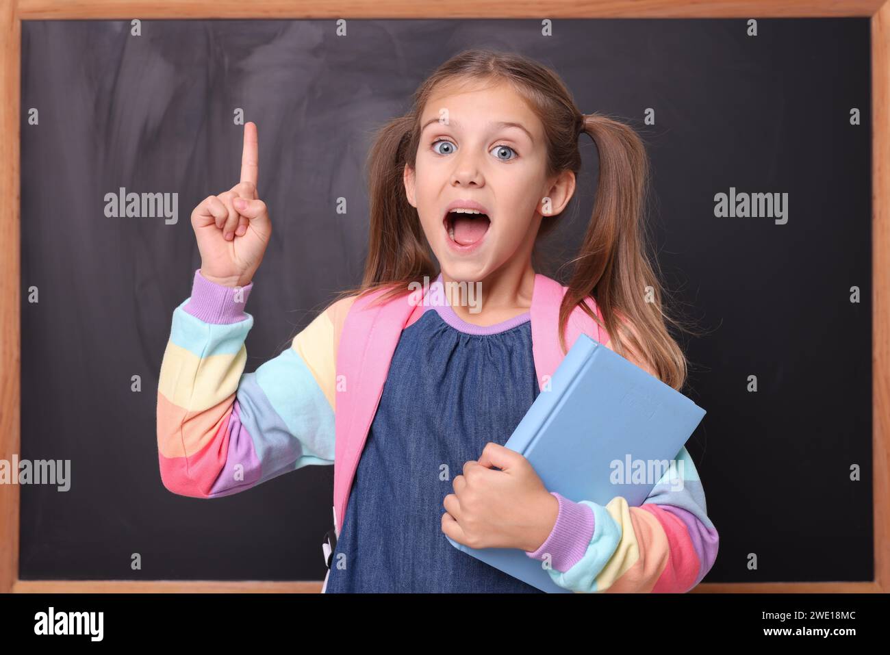 Pointing Near Excited schoolgirl with book pointing at something near blackboard ...