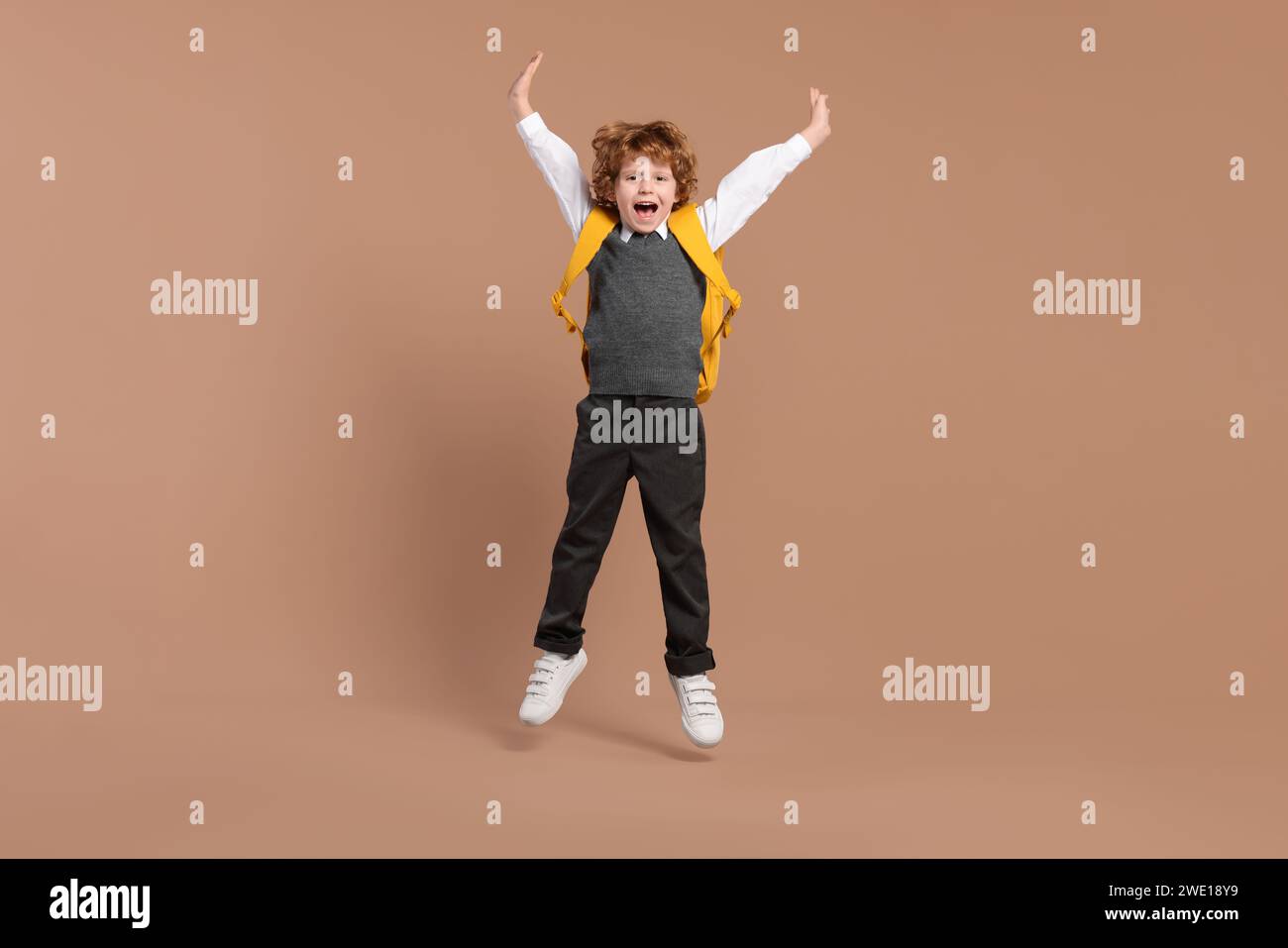 Happy schoolboy with backpack jumping on brown background Stock Photo ...