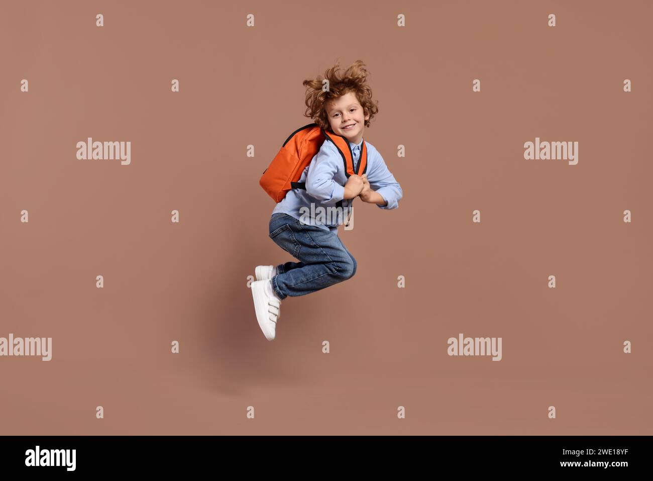 Happy schoolboy with backpack jumping on brown background Stock Photo ...