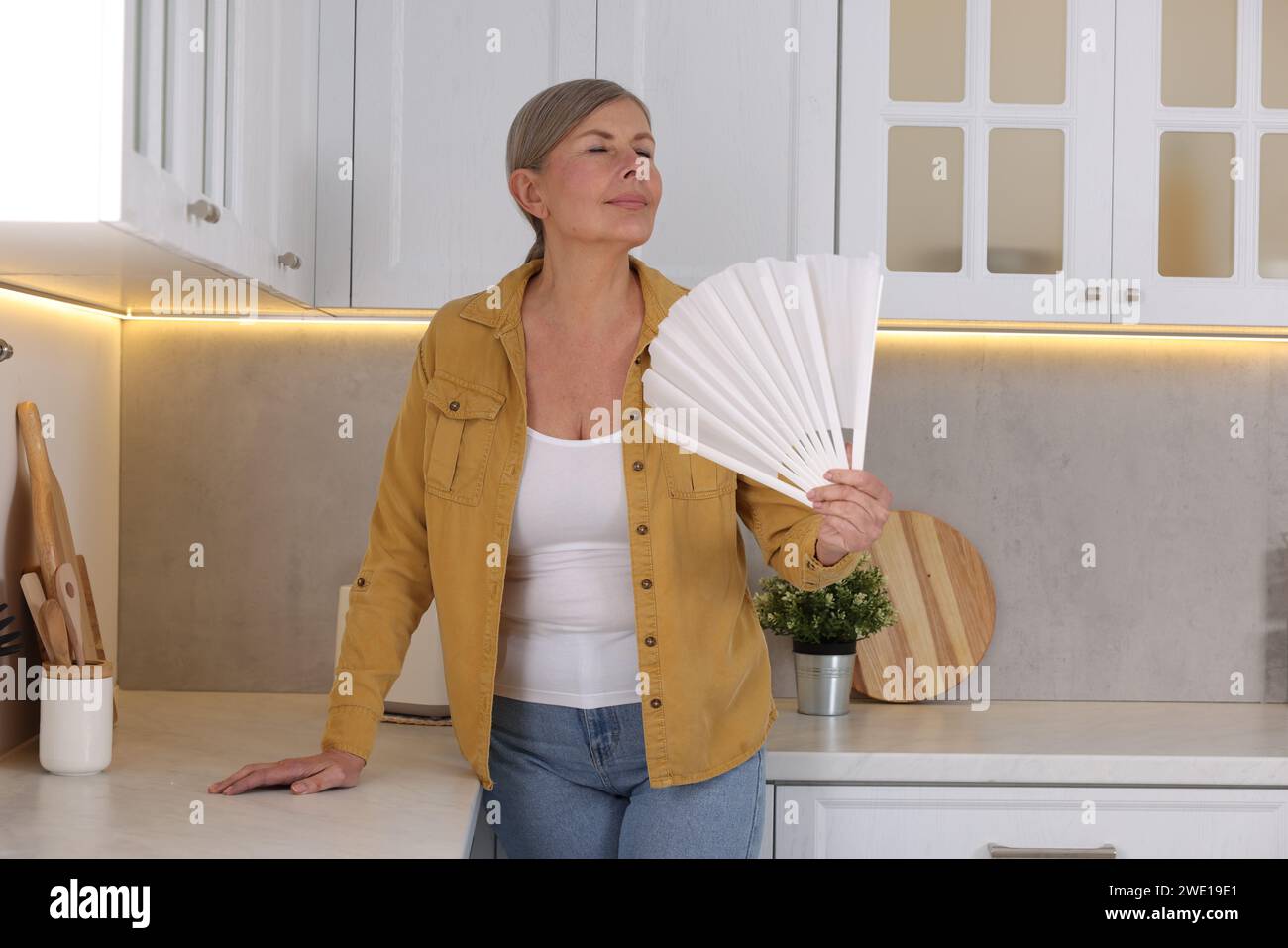 Menopause. Woman waving hand fan to cool herself during hot flash in