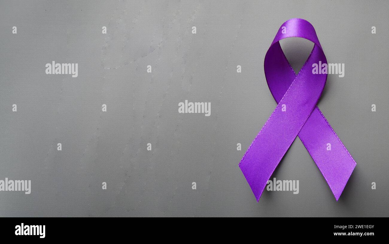 A hand holding luxury purple ribbon on a gray background. Purple ribbon with pancreatic cancer awareness. Stock Photo