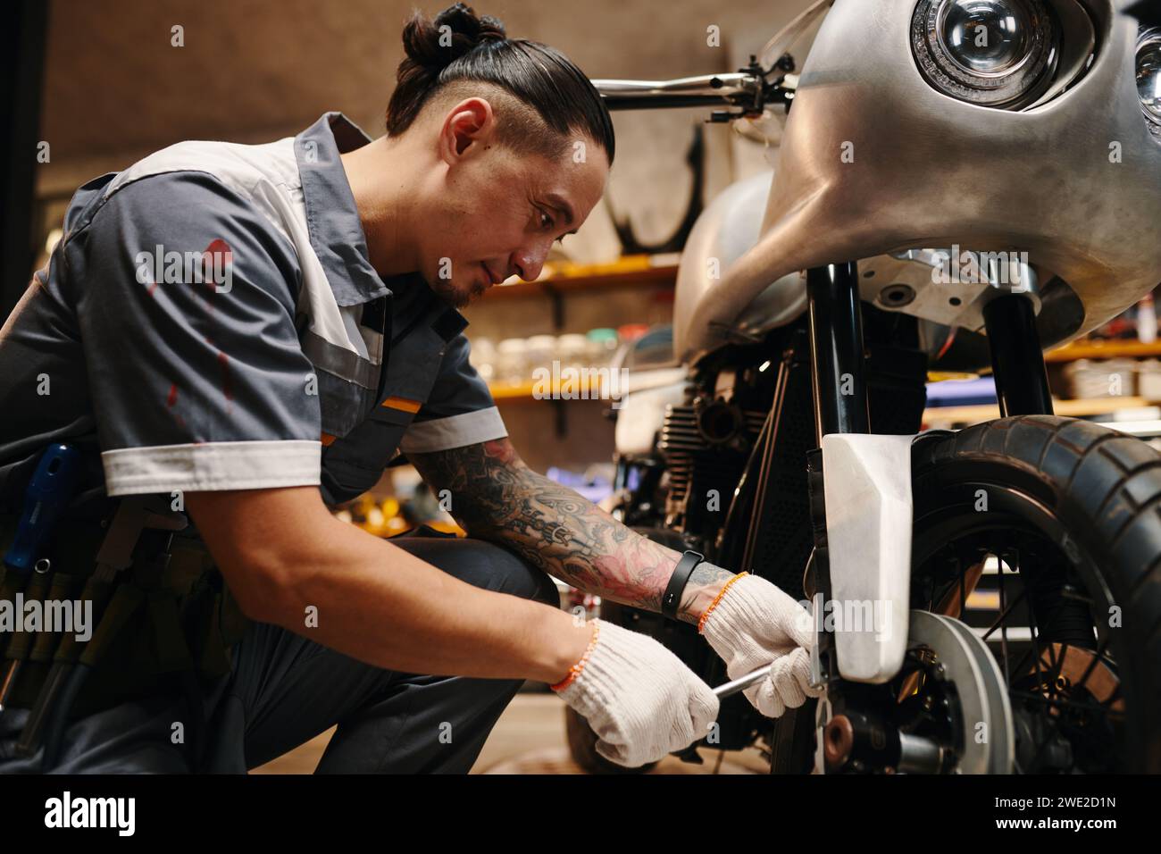 Mechanic in uniform fixing wheel of motorcycle Stock Photo - Alamy