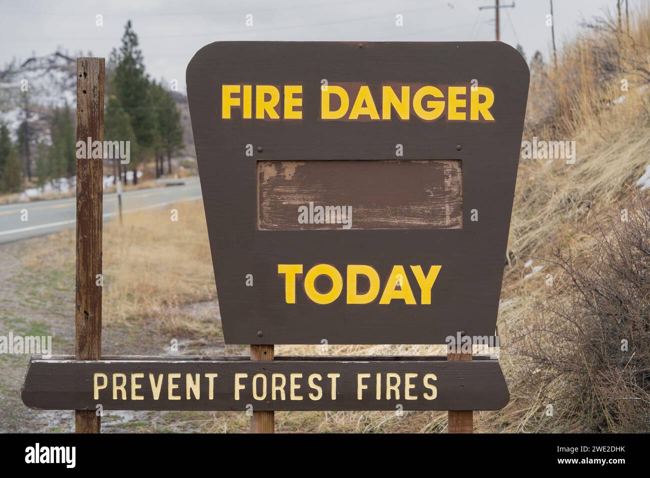 Blank 'Fire Danger Today Prevent Forest Fires' sign in winter surrounded by patchy snow and wet conditions near road (close-up). Stock Photo