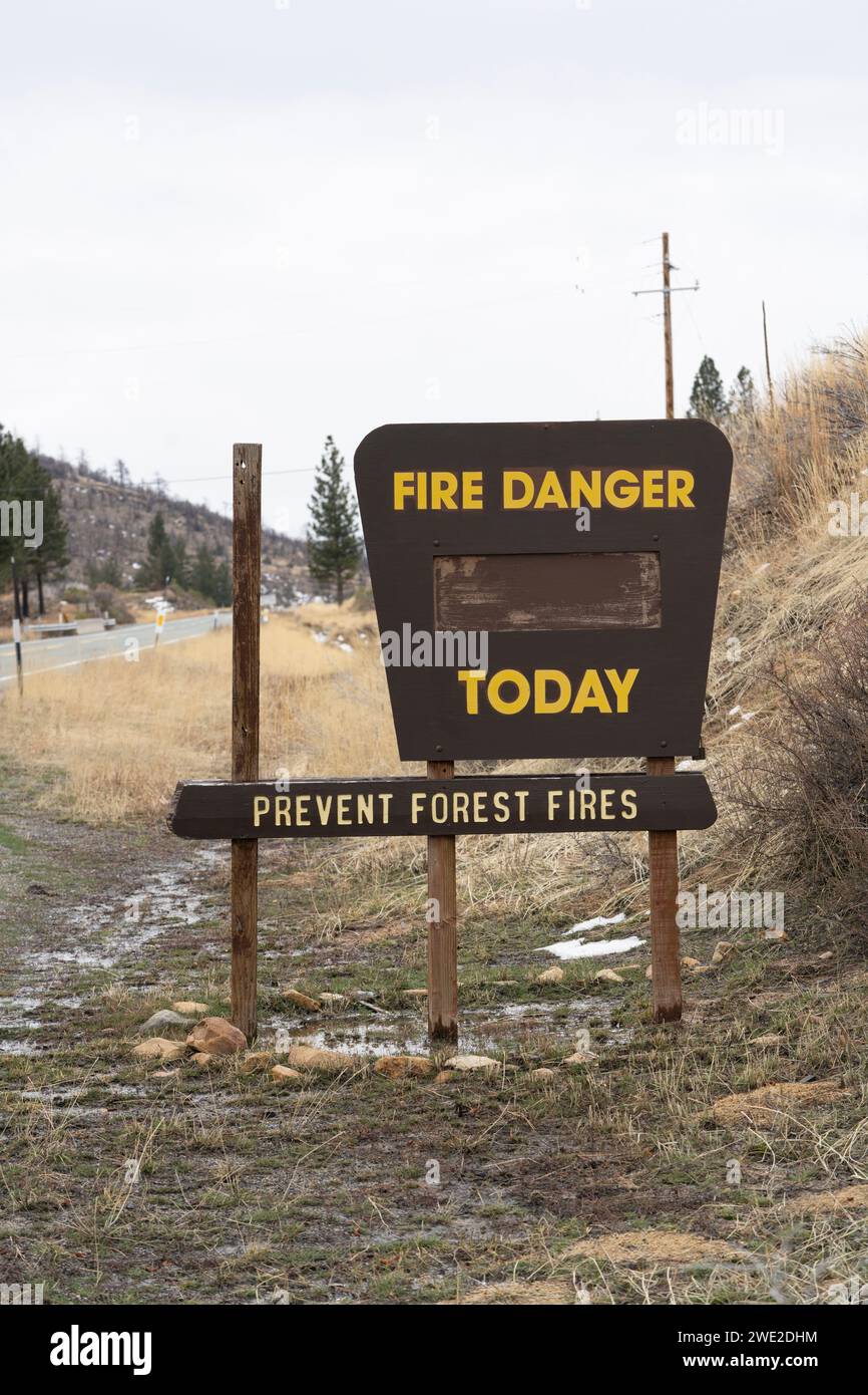 Blank 'Fire Danger Today Prevent Forest Fires' sign in winter surrounded by patchy snow and wet conditions near road (vertical). Stock Photo