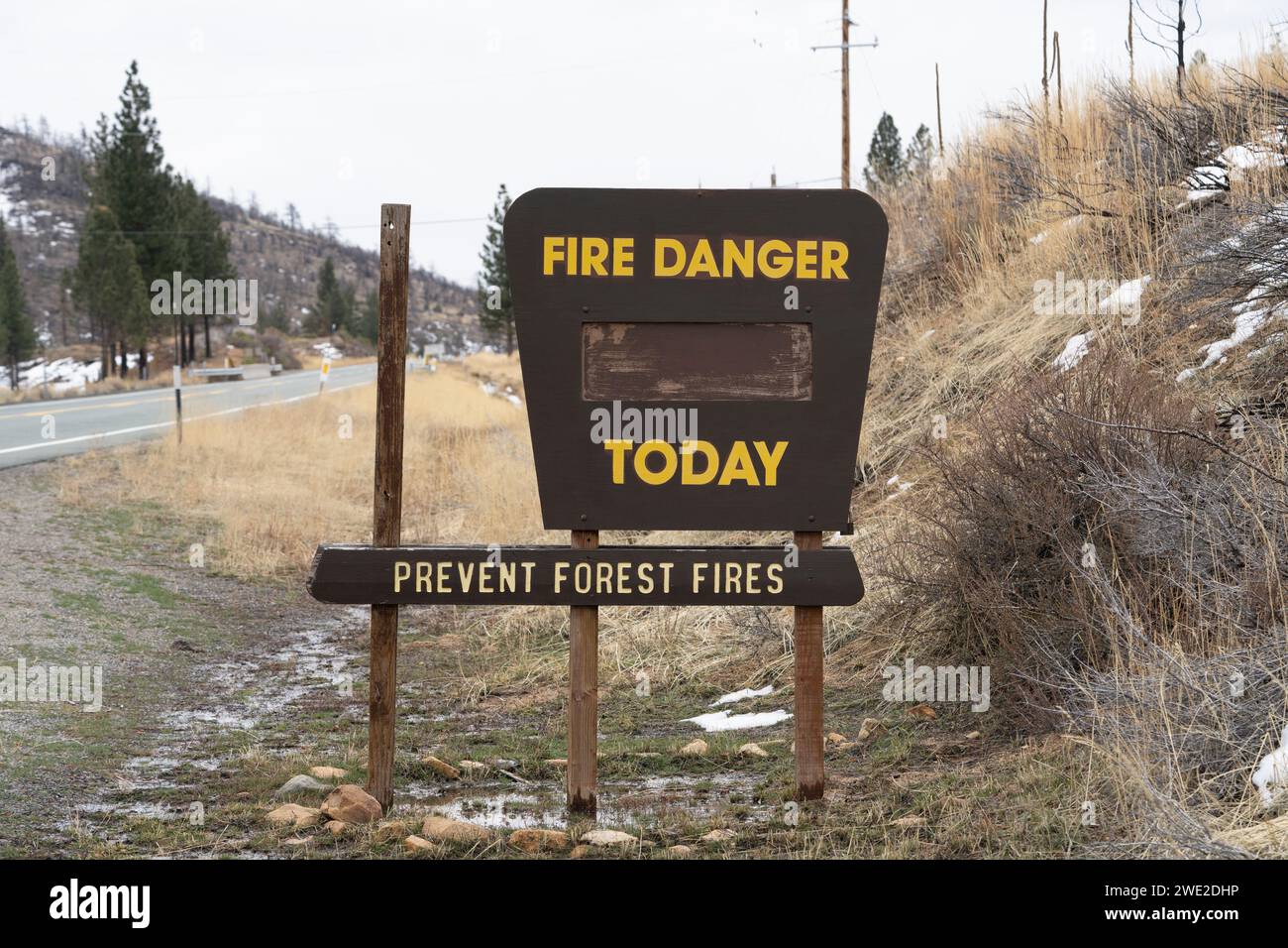 Blank 'Fire Danger Today Prevent Forest Fires' sign in winter surrounded by patchy snow and wet conditions near road. Stock Photo