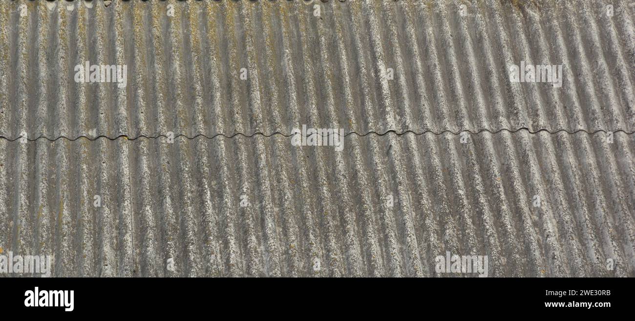 Old corrugated asbestos roof tile background with a copy space. A close-up of asbestos cement roofing sheathing of a gable roof. Stock Photo