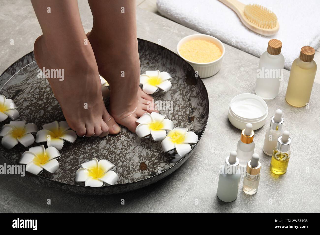 Woman soaking her feet in bowl with water and flowers on light grey floor, closeup. Spa treatment Stock Photo