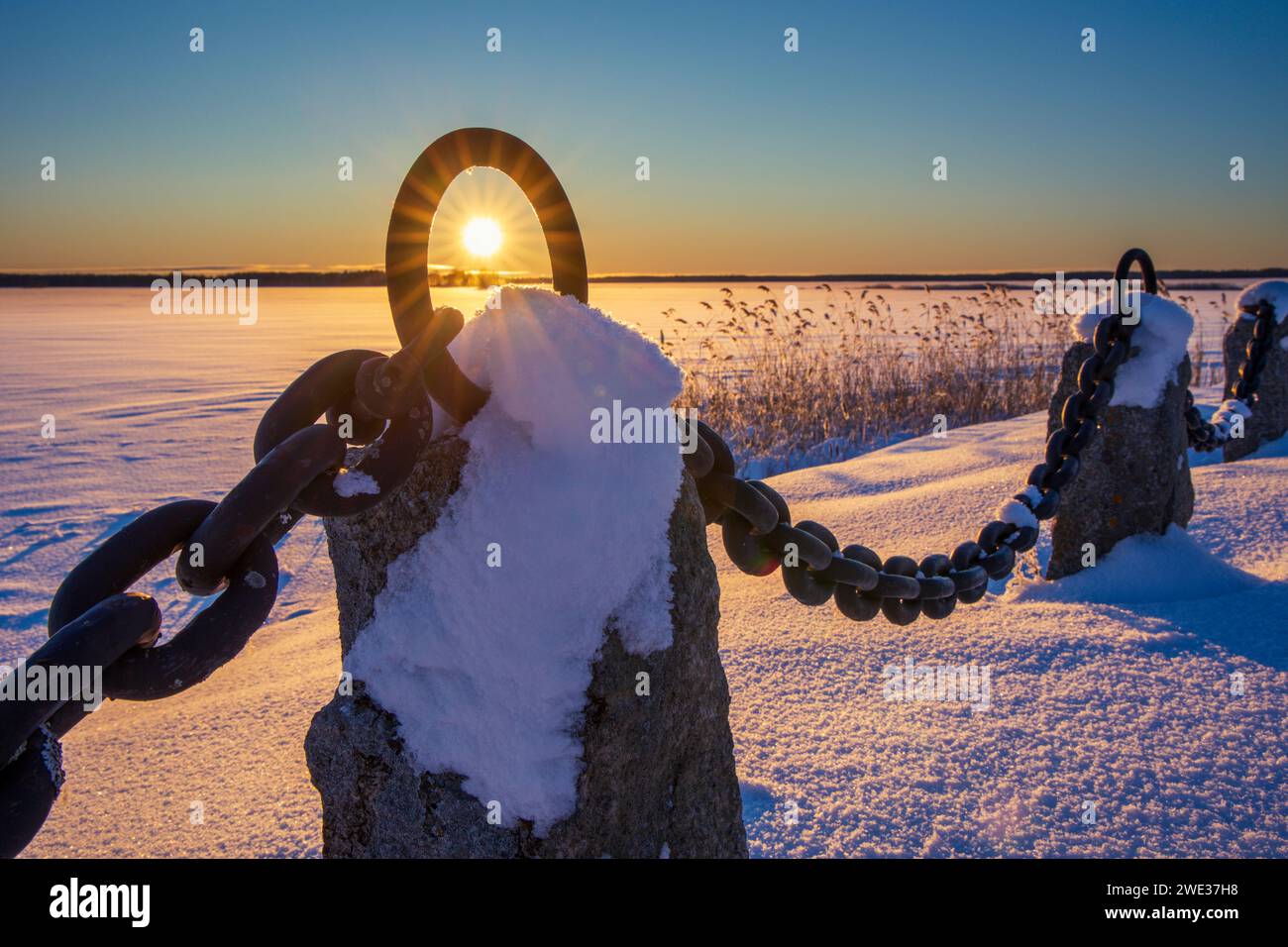 A beautiful sunset over a snow-covered field with a chain in the foreground. Sandviken, Sweden Stock Photo