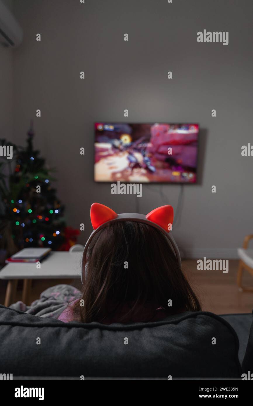 Back view of a child girl sitting on the couch and playing video game ...