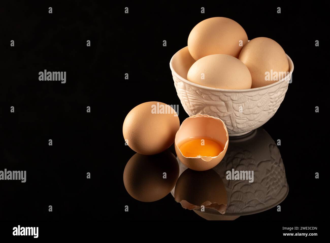 A group of raw, uncooked brown chicken eggs are neatly arranged on a shiny, black reflective surface, creating an ideal setup for engaging food photog Stock Photo