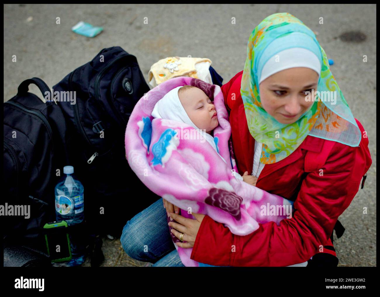 Image ©Licensed to Parsons Media. 22/09/2015.Croatia. Migrants in Croatia. Migrant children.   Croatia. Migrant Haila wipes away a tear with her daughter Lilas 9 months, sitting on the road outside the gates of a  refugee camp in Opatovac, Croatia, after just crossing the Serbian Border  Picture by Andrew Parsons / Parsons Media Stock Photo