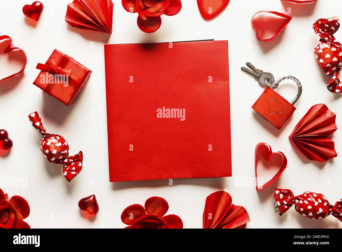 Valentine's day flat lay frame with red blank greeting card and hearts, flowers, candies and little gift box scattered on a white background, top view Stock Photo