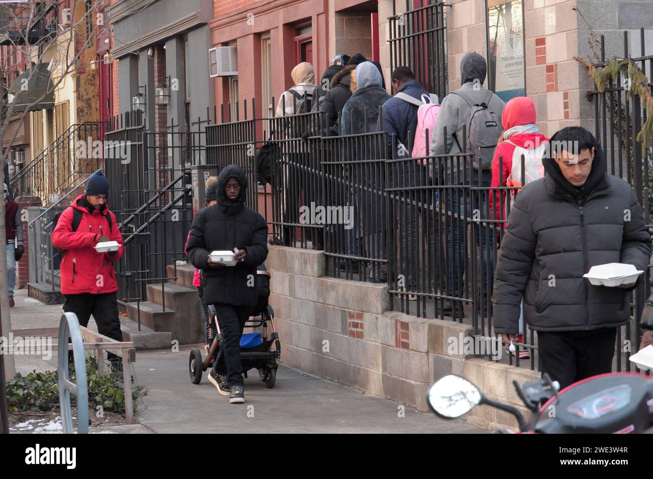 New York, United States. 22nd Jan, 2024. Migrants wait in a line to receive food. Single adult migrants who were authorized by New York City to leave the shelter system after 30 days, wait in line outside of a closed down St. Brigid School in the East Village. The former school serves as a re-intake center for migrants seeking relocation to another shelter. The migrants have been waiting outside in the freezing winter temperature as aid groups have been donating food and clothing. Credit: SOPA Images Limited/Alamy Live News Stock Photo