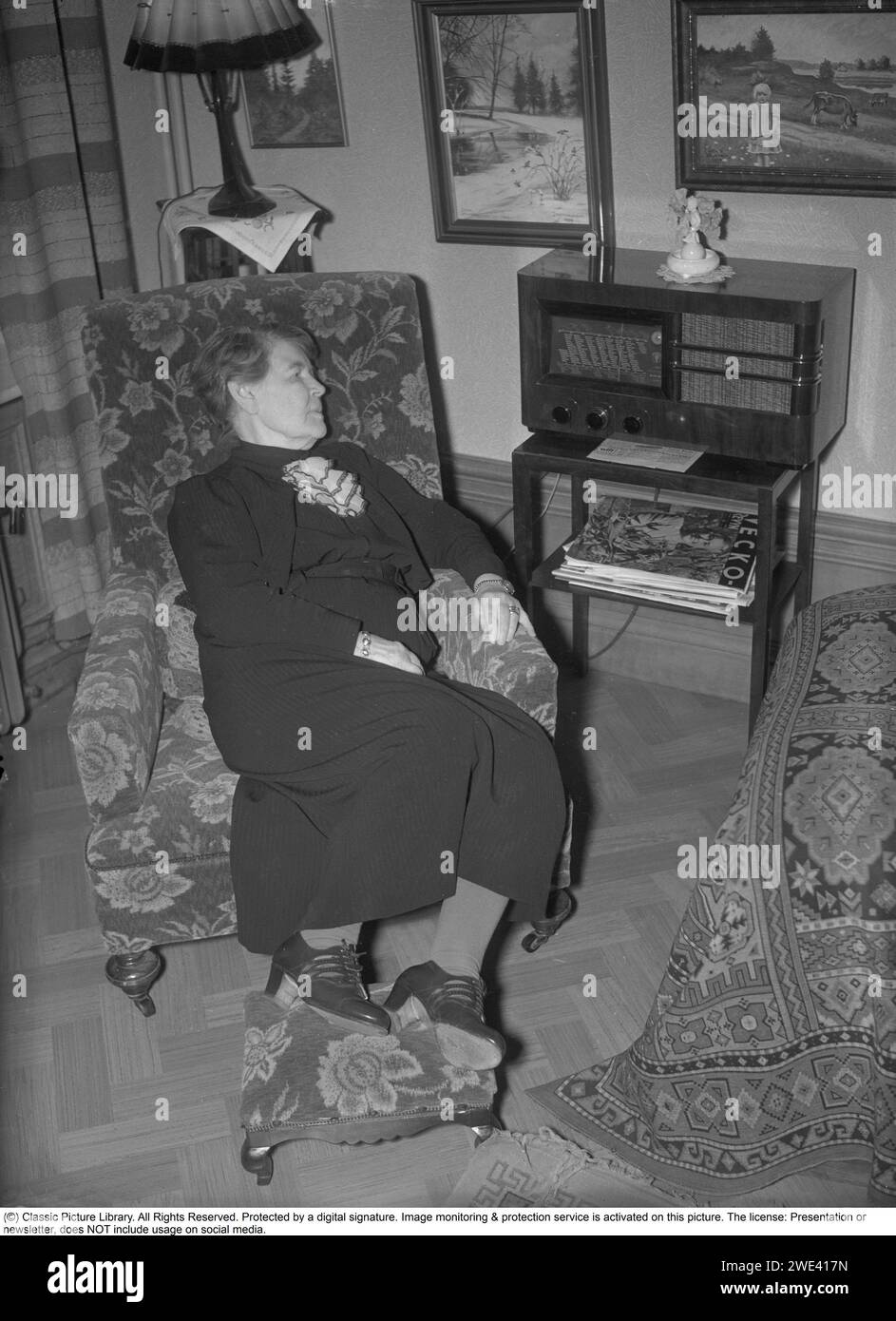 Radio in the 1930s. An elderly woman is listening to the radio.  In addition to FM broadcasts from local radiostations, foreign radio stations were also listened to on longwave. She is famous swedish illustrator Jenny Nyström, 1854-1946, known for her paintings of santa claus on millions of christmas cards.  17 november 1939. Krisotffersson ref 6-9 Stock Photo