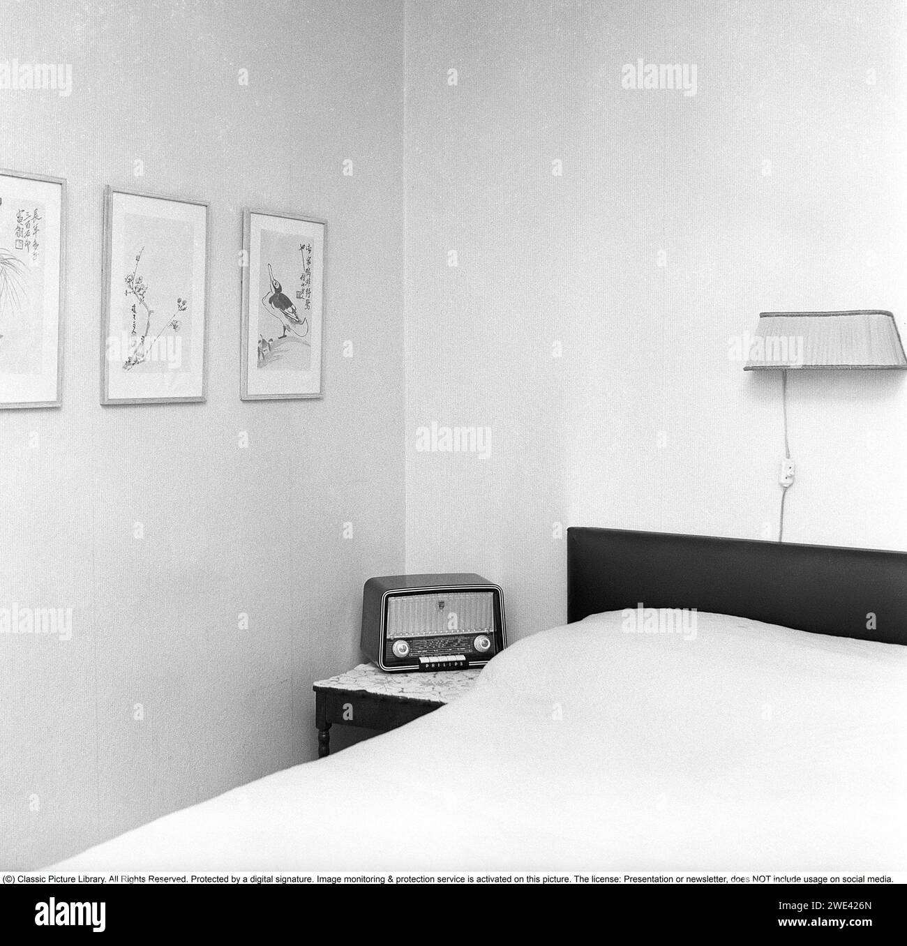 In the 1950s. Interior of a bedroom with a Philips radio standing on the small table on the side of the bed. 1956. Svahn ref SVA1 Stock Photo