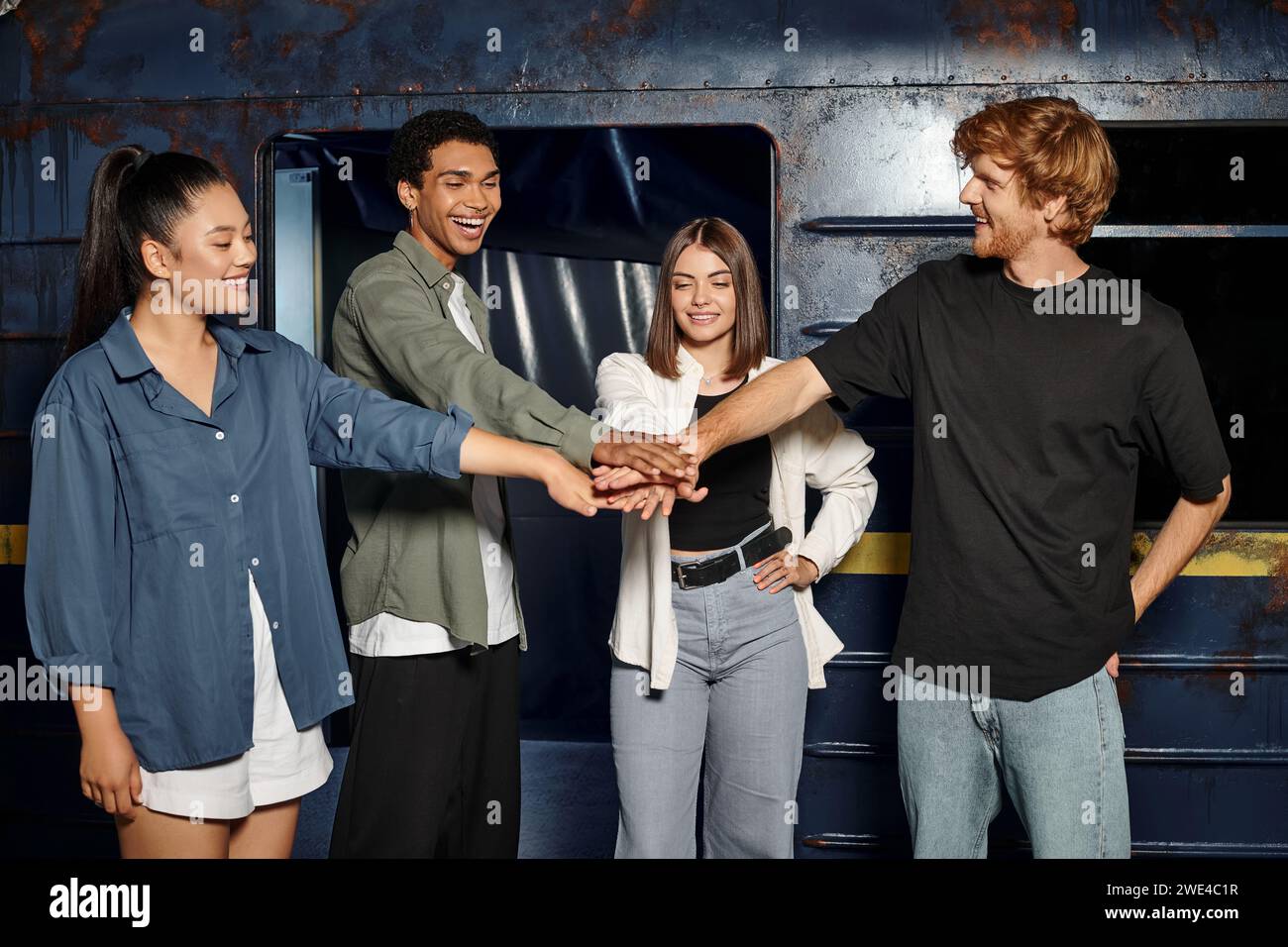 group of happy multicultural friends staking hands together before quest room game in subway setting Stock Photo