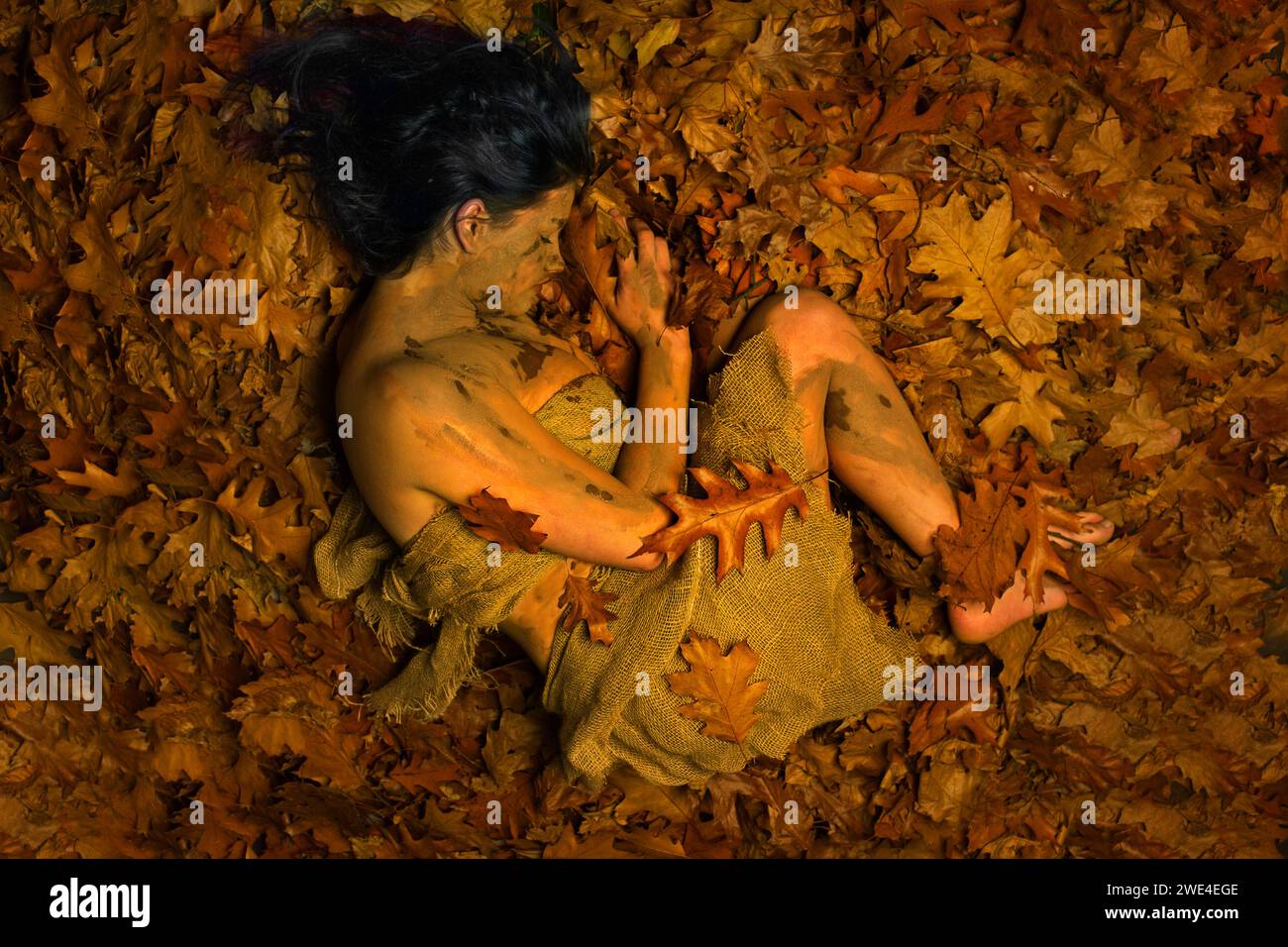 Girl lying on a bed of leaves coverd in mud Stock Photo