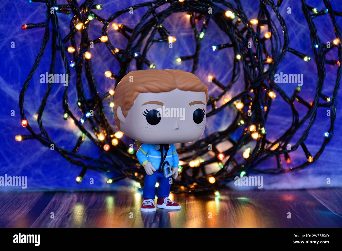 Funko Pop action figure of Max Mayfield with cassette player from TV series Stranger Things. Blue foggy background, colorful lights, mysterious place. Stock Photo