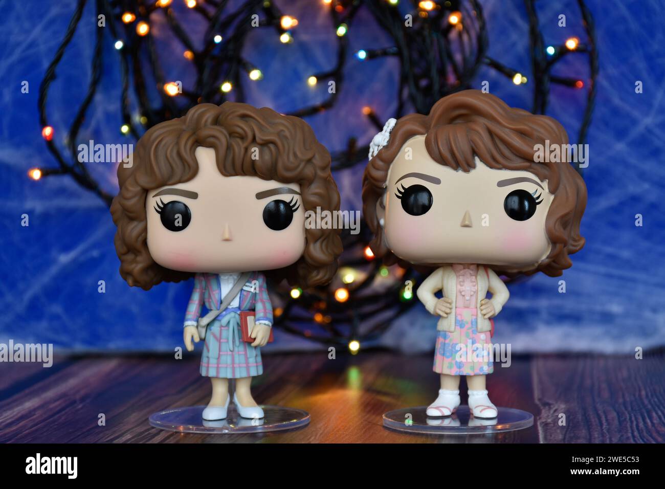 Funko Pop action figures of Nancy and Robin as academics from Netflix TV series Stranger Things. Blue foggy background, colorful lights, mysterious. Stock Photo