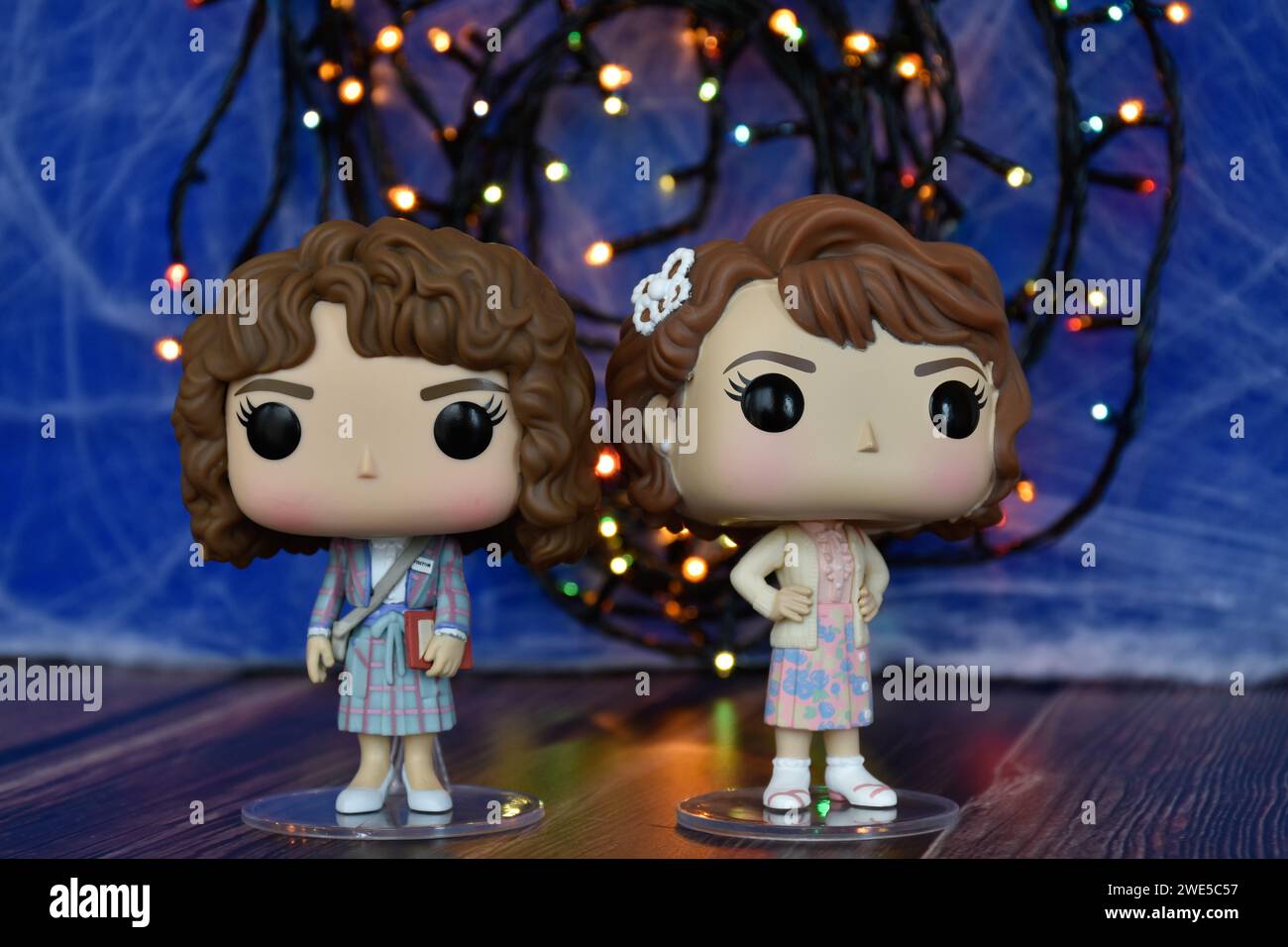 Funko Pop action figures of Nancy and Robin as academics from Netflix TV series Stranger Things. Blue foggy background, colorful lights, mysterious. Stock Photo