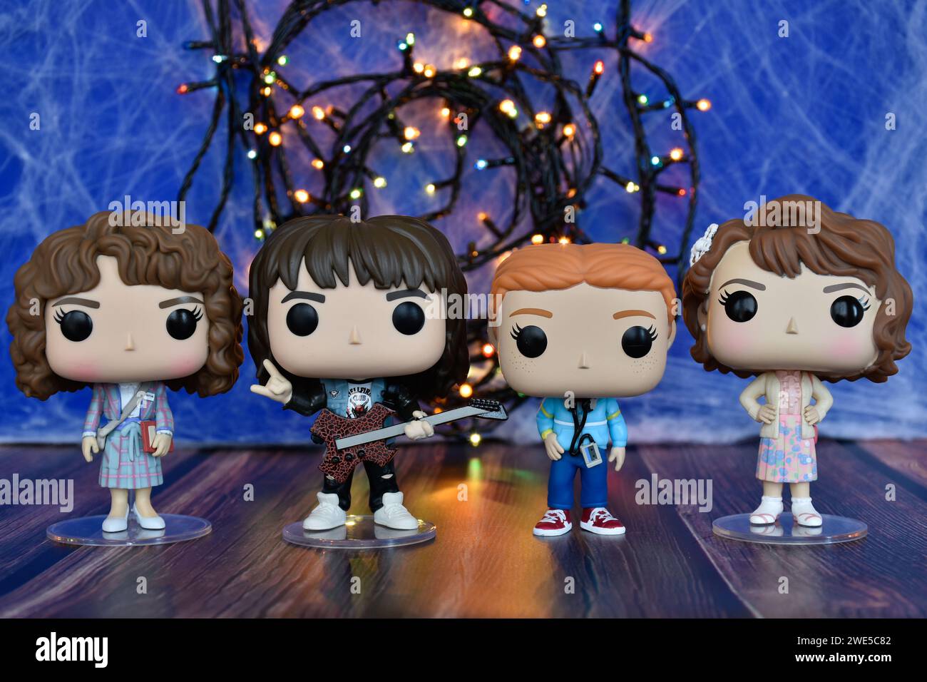 Funko Pop action figures of Nancy, Eddie, Max and Robin from TV series Stranger Things, season 4. Blue foggy background, colorful lights, mysterious. Stock Photo