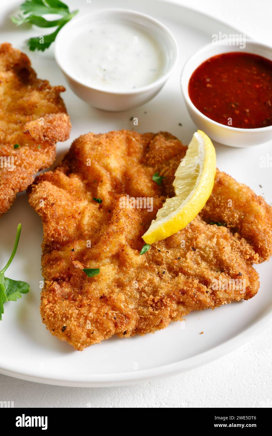 Breaded wiener schnitzel served with sauce on white plate over light background. Close up view Stock Photo