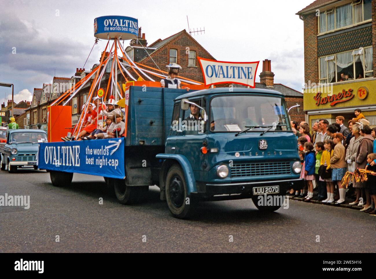 Watford's annual Whitsun Carnival parade proceeding along St Albans Road, Watford, Hertfordshire, England, UK, 1967. On the rear of Bedford flatbed lorry children promote bedtime drink Ovaltine, invented Switzerland 1904 by Doctor George Wander and launched in UK in 1909. A banner on side of truck states Ovaltine: the world's best night-cap. This image is from an old amateur Kodak colour transparency – a vintage 1960s photograph. Stock Photo