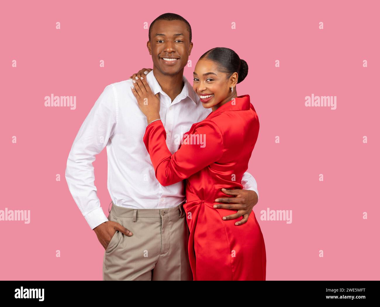 Smiling black couple embracing, woman in red dress, man in white shirt, pink background Stock Photo