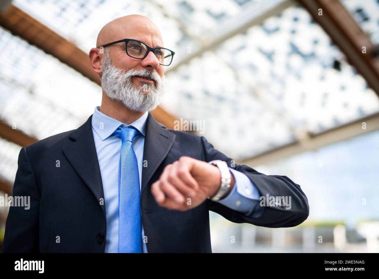 Smiling businessman checking his wrist watch while waiting for someone Stock Photo