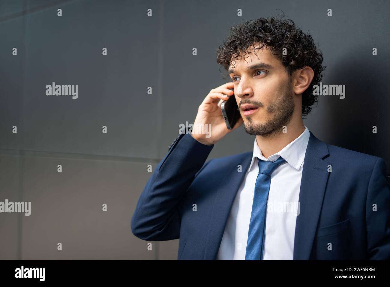 Young businessman standing next to a black wall while talking on the phone Stock Photo