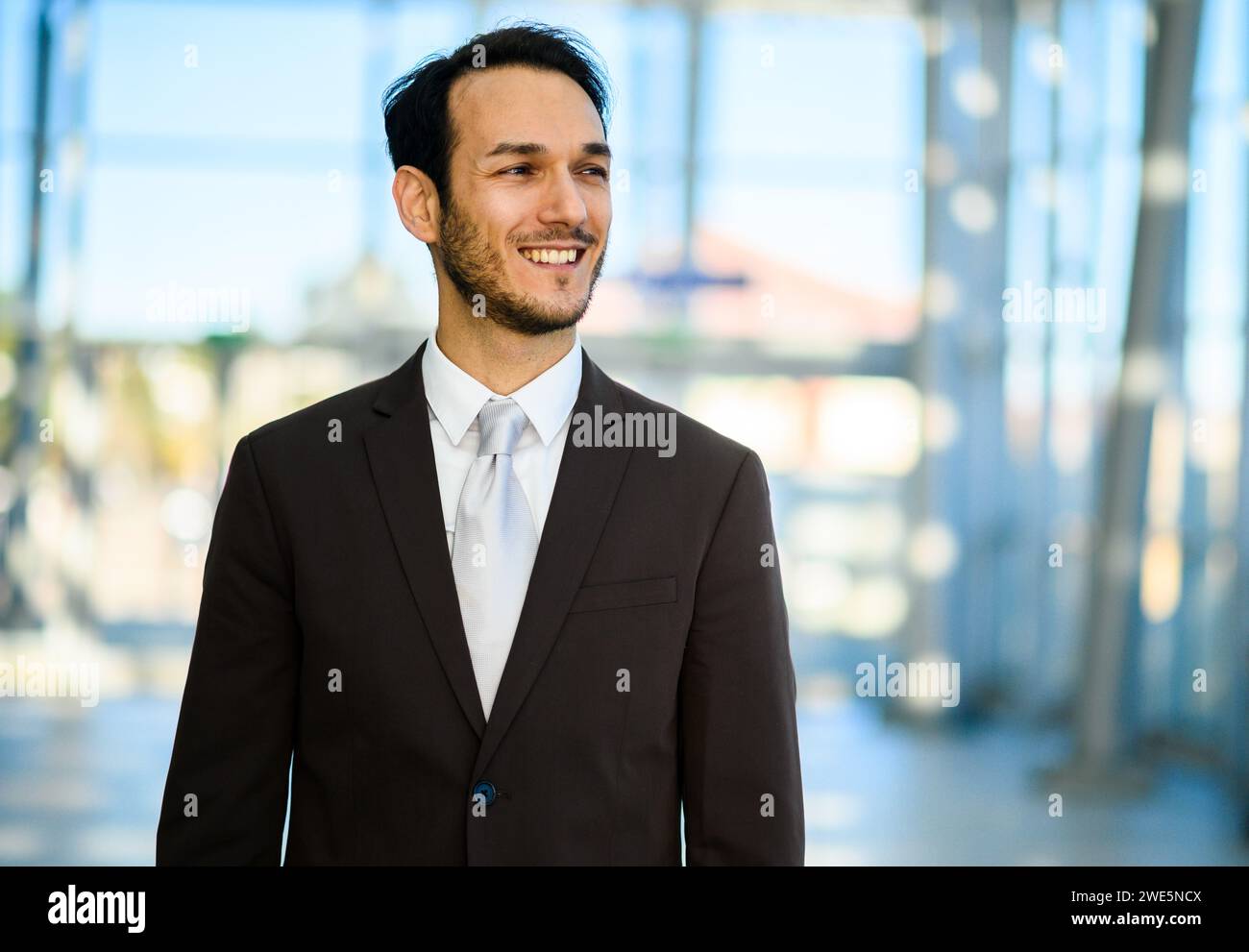 Young adult male businessman in a stylish, modern suit confidently smiling outdoors, showcasing his successful career and leadership in the corporate Stock Photo