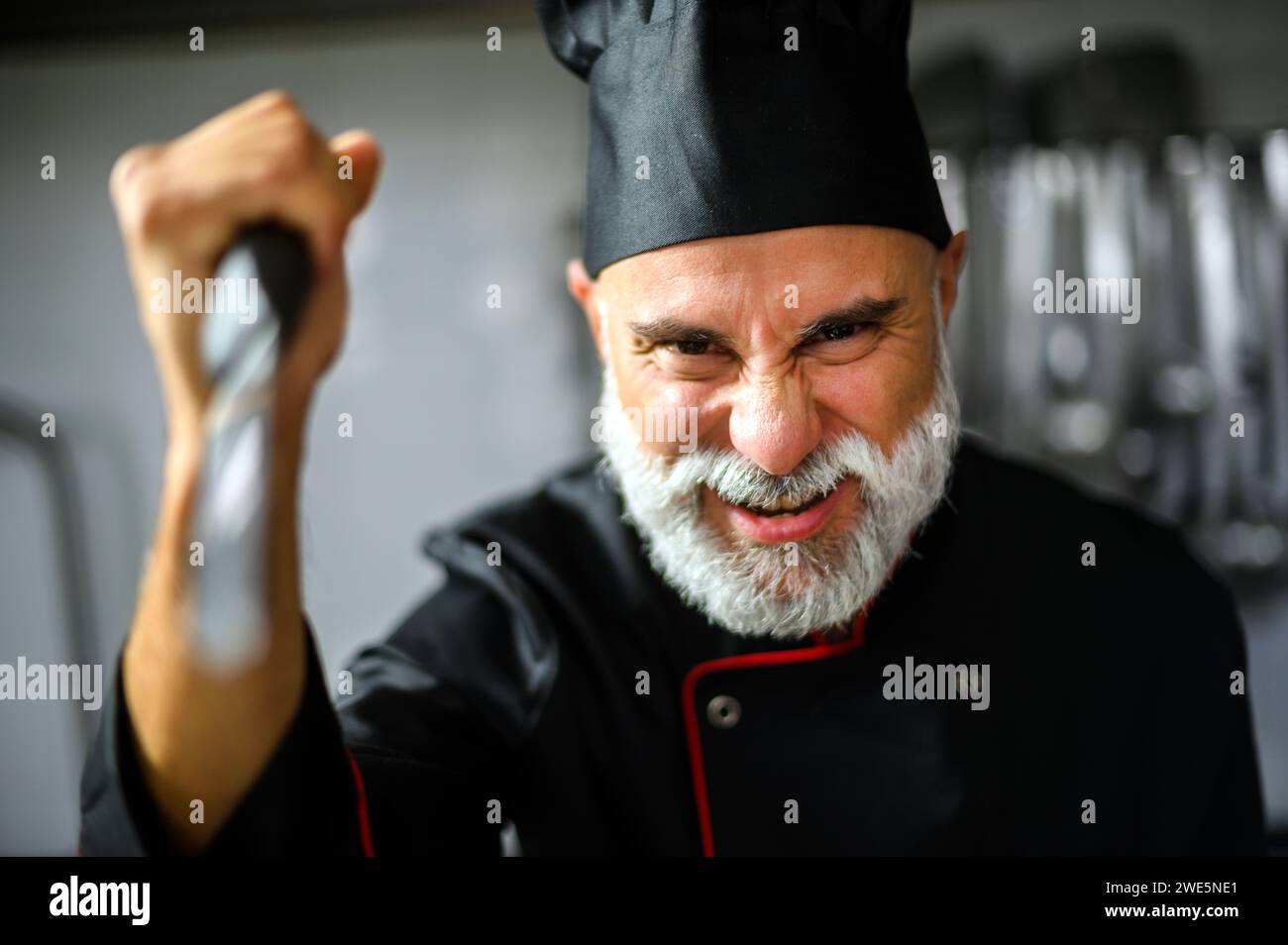 Intense male chef wearing uniform, showing frustration in a professional kitchen setting Stock Photo