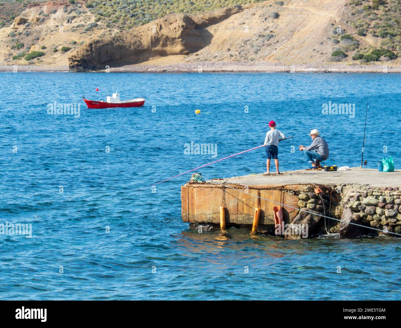 Older man teaching his grandson to fish on a pier on the coast of Cabo de Gata, Almeria. Stock Photo