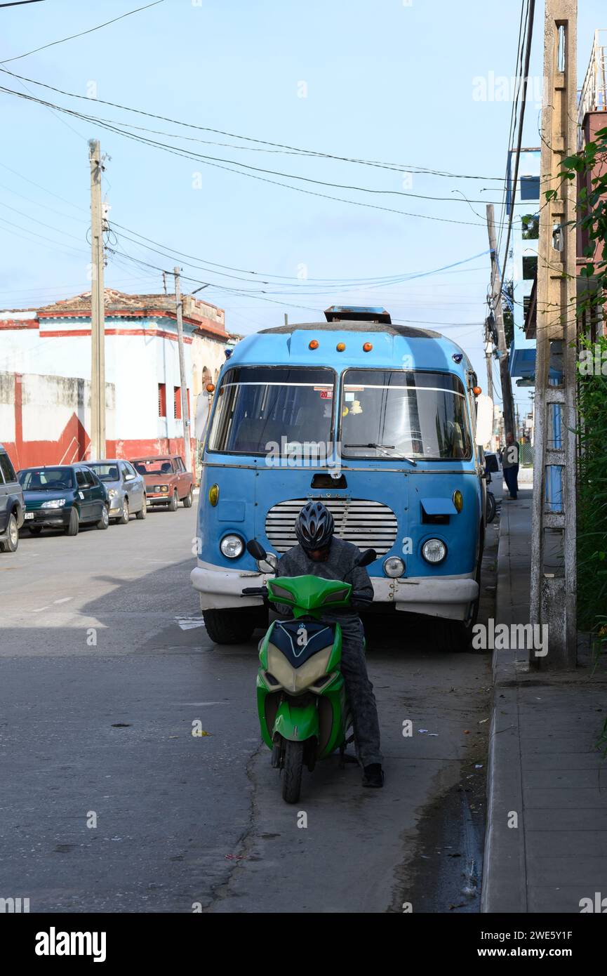 A man in an electric bicycle is parked in front of a vintage obsolete bus in Maceo Street Stock Photo