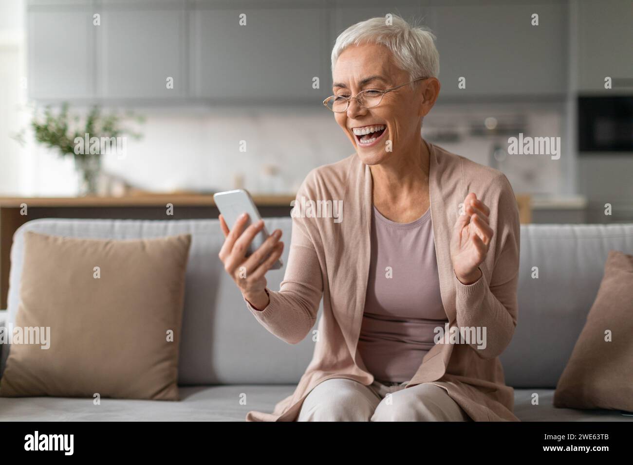 Cheerful senior woman using smartphone and having fun at home Stock Photo