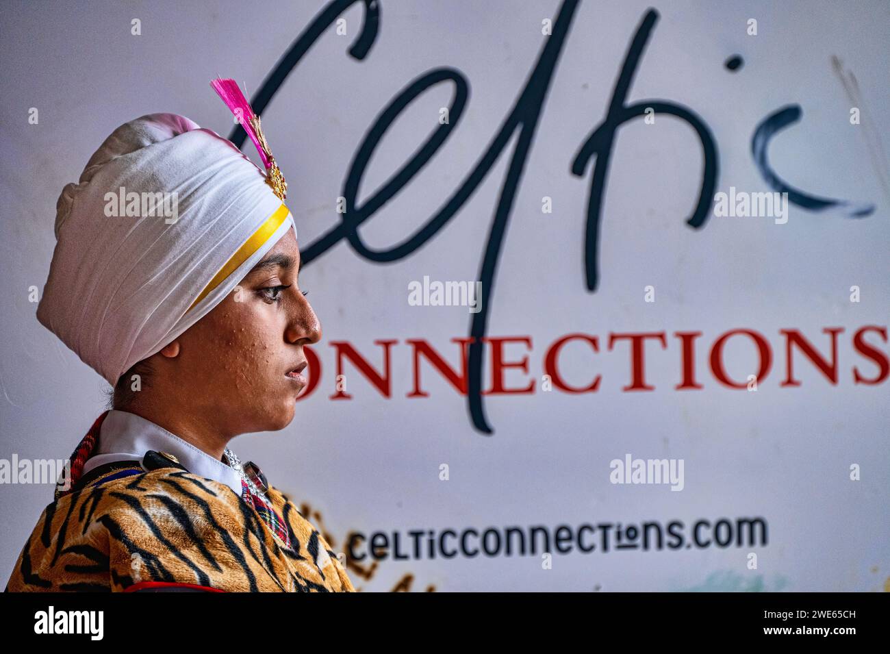 Female drummer from the Sri Dasmesh Malaysian Pipe Band takes a break in front of poster advertising Celtic Connections series ofconcerts. Stock Photo