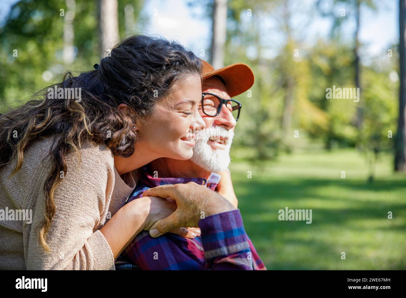 Happy caregiver embracing retired senior man at park Stock Photo