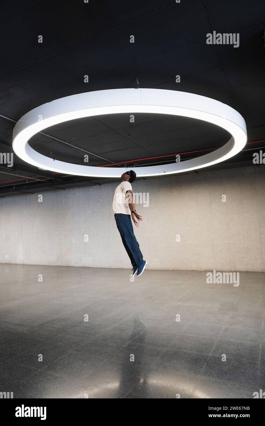 Young man with futuristic cyber glasses jumping under modern ring lamp Stock Photo