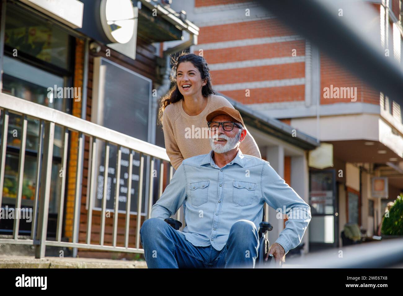 Happy volunteer pushing retired man in wheelchair by railing Stock ...