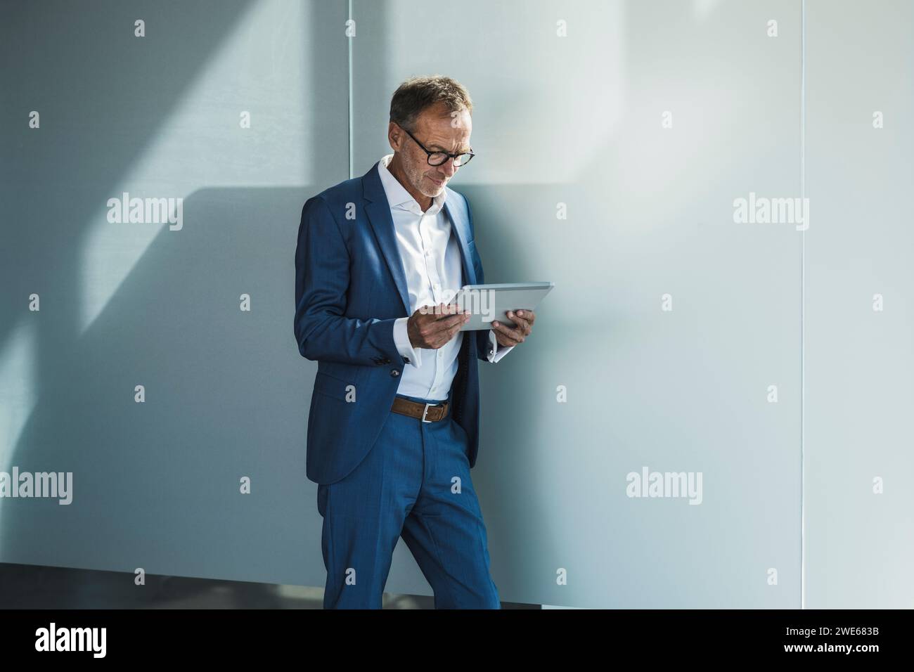 Businessman using tablet PC and leaning on wall Stock Photo