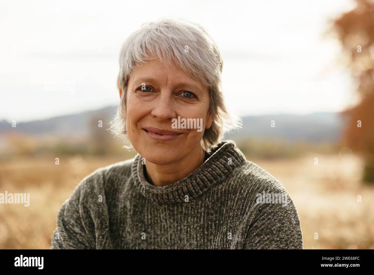 Smiling mature woman with gray hair under sky Stock Photo