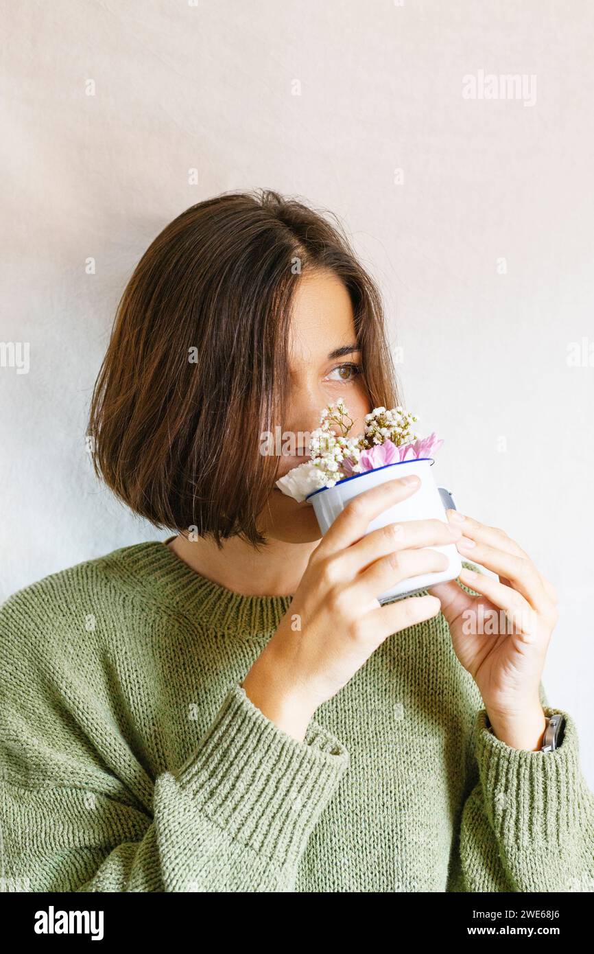 Beautiful woman smelling flowers from mug against white background Stock Photo