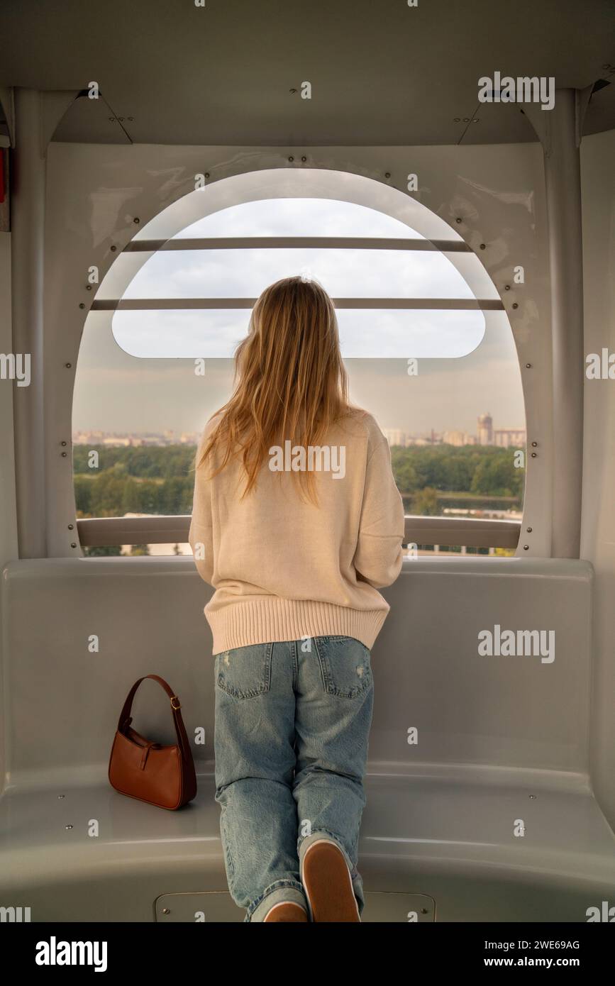 Woman kneeling on seat and looking through Ferris wheel window Stock Photo