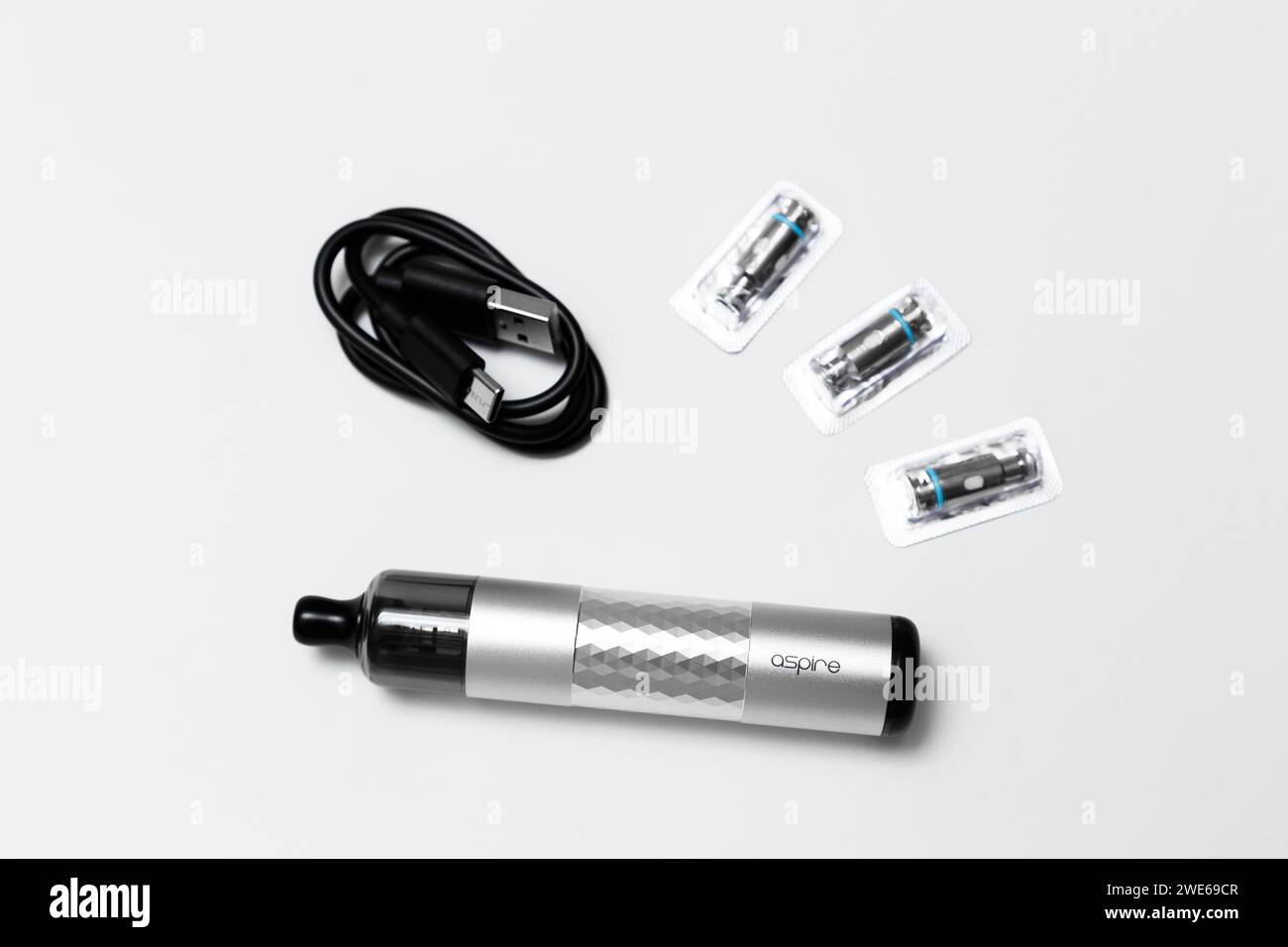 Ukraine, Odesa - January, 4 2024: Vaping device, vape Aspire Flexus Stik Pod Kit silver color with charging cable USB Type-C and mesh coils on white background, top view. Stock Photo