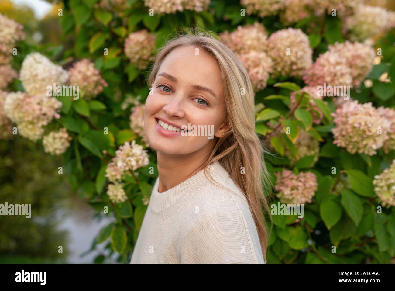 Happy blond woman in front of flowering plant Stock Photo