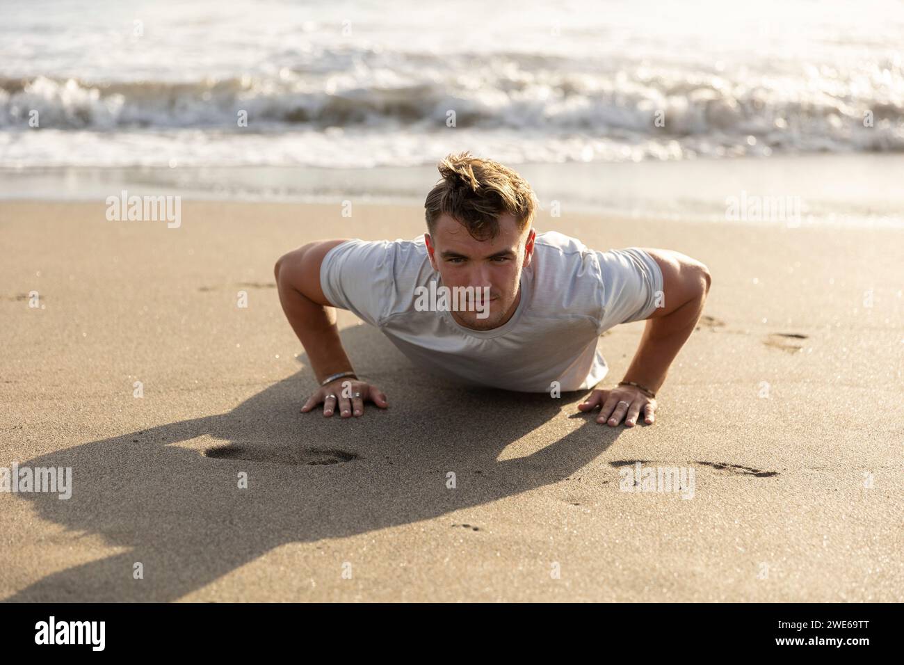 Man doing push-ups on sand at beach Stock Photo