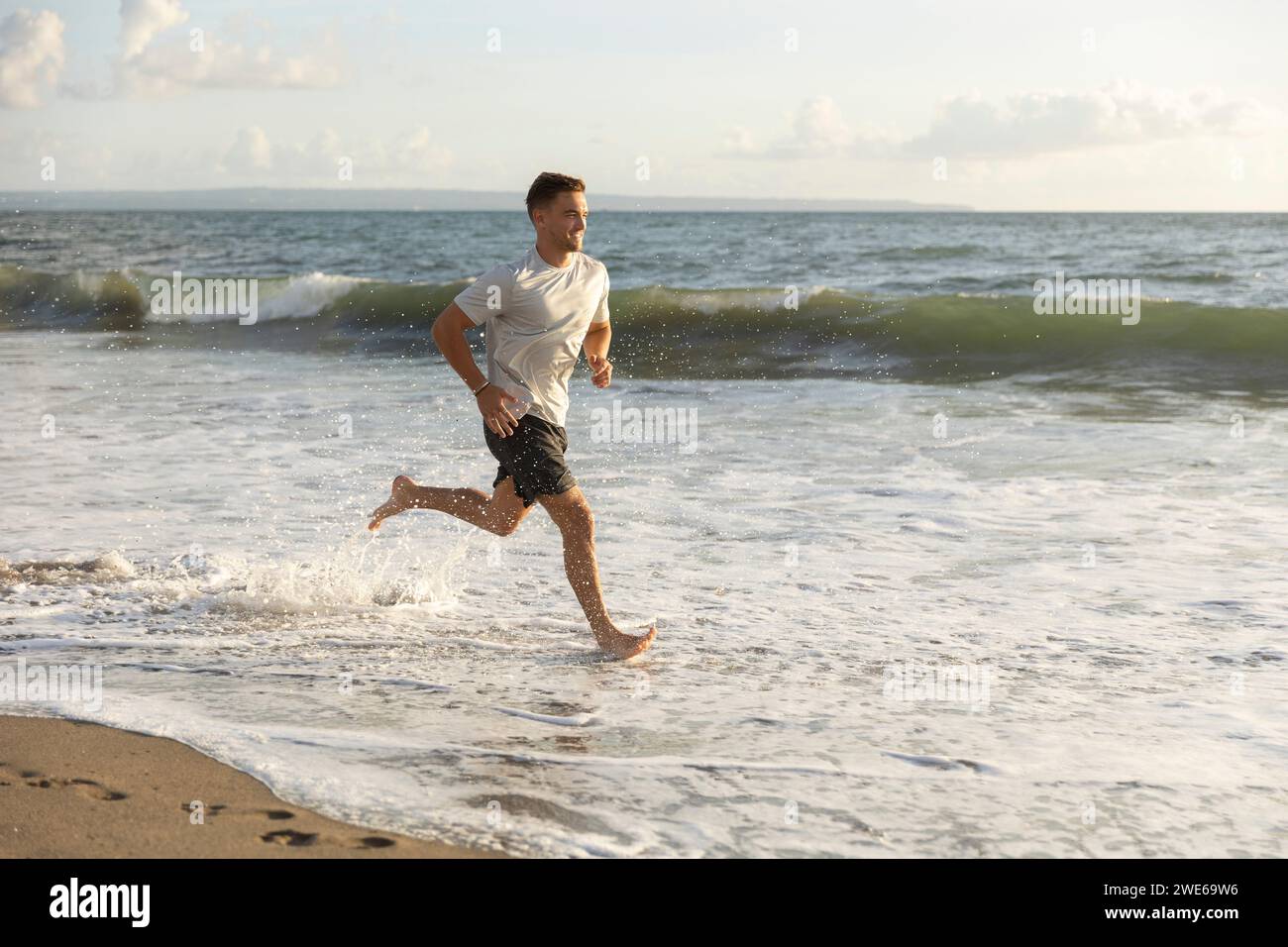 Smiling young man running in water at beach Stock Photo