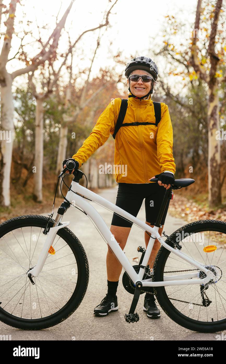 Smiling woman standing with mountain bike on road in forest Stock Photo