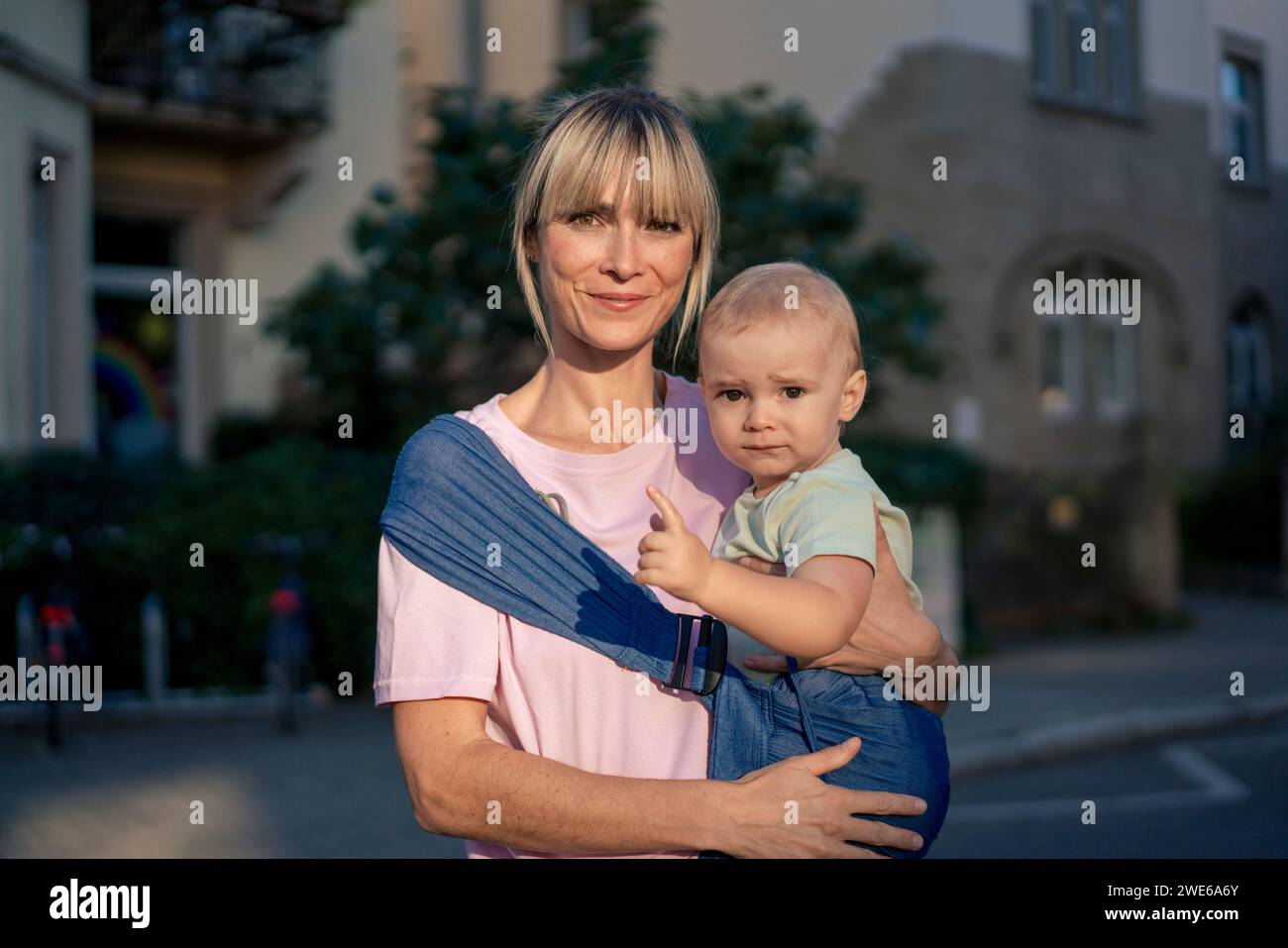 Smiling woman carrying son in baby sling Stock Photo